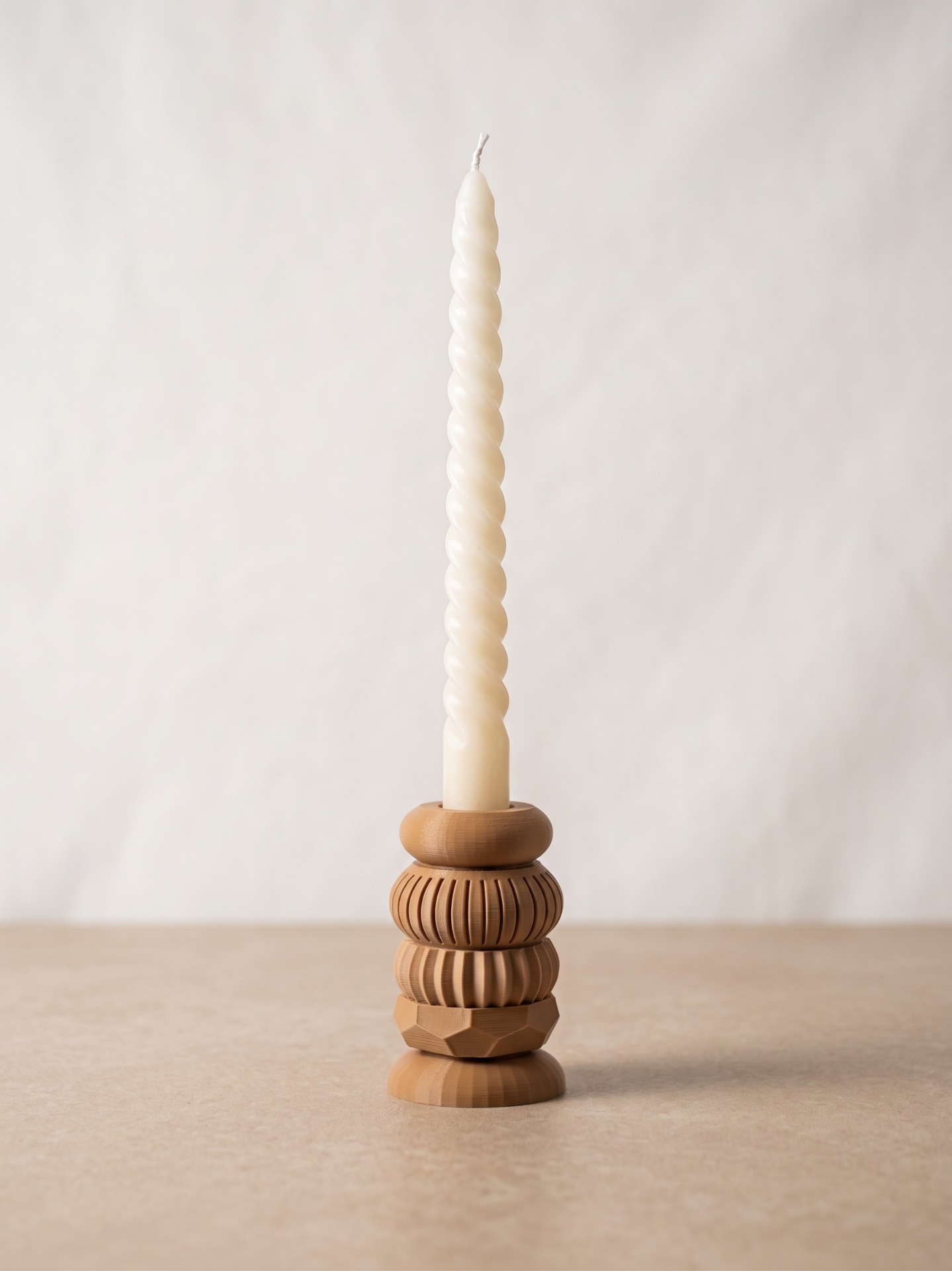 Witte gedraaide kaars op houten voet, tegen egale achtergrond, minimalistische studio-opname.